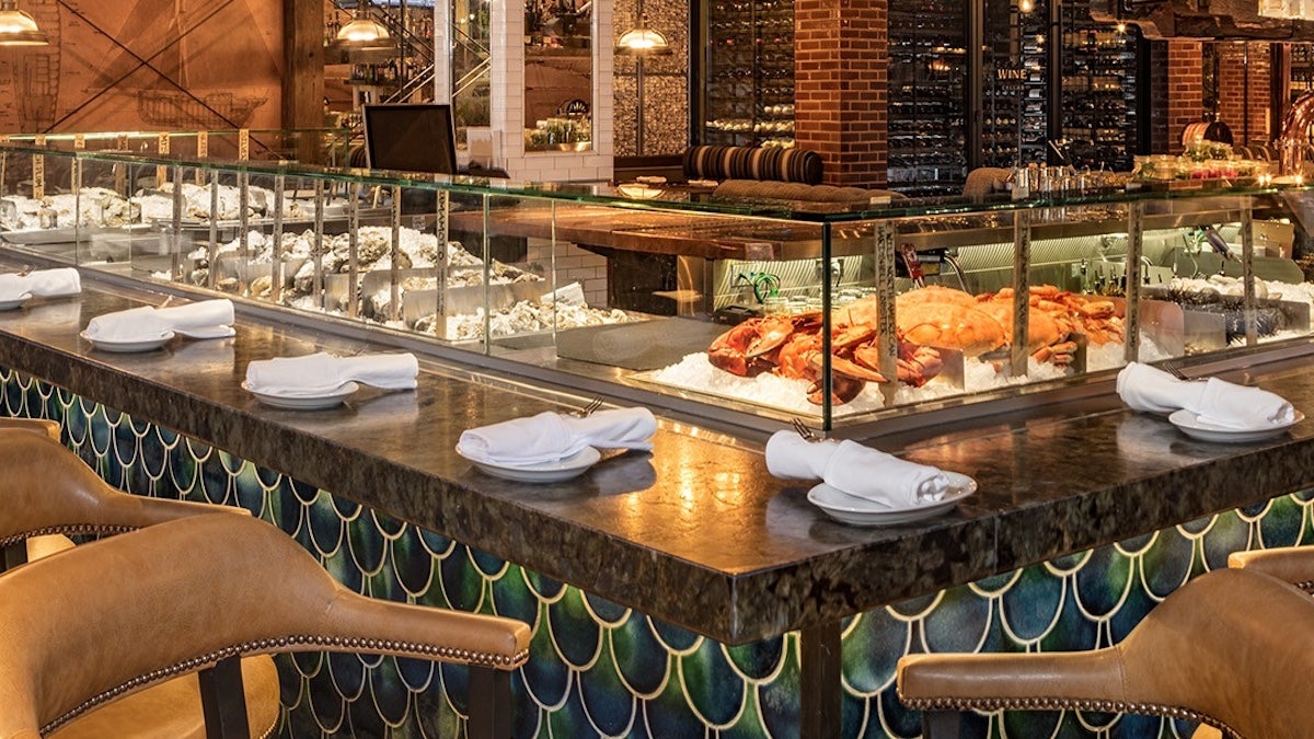 Interior of Water Grill San Diego featuring a seafood bar with a glass display of fresh oysters and lobsters on ice, surrounded by upscale leather chairs and elegant decor.